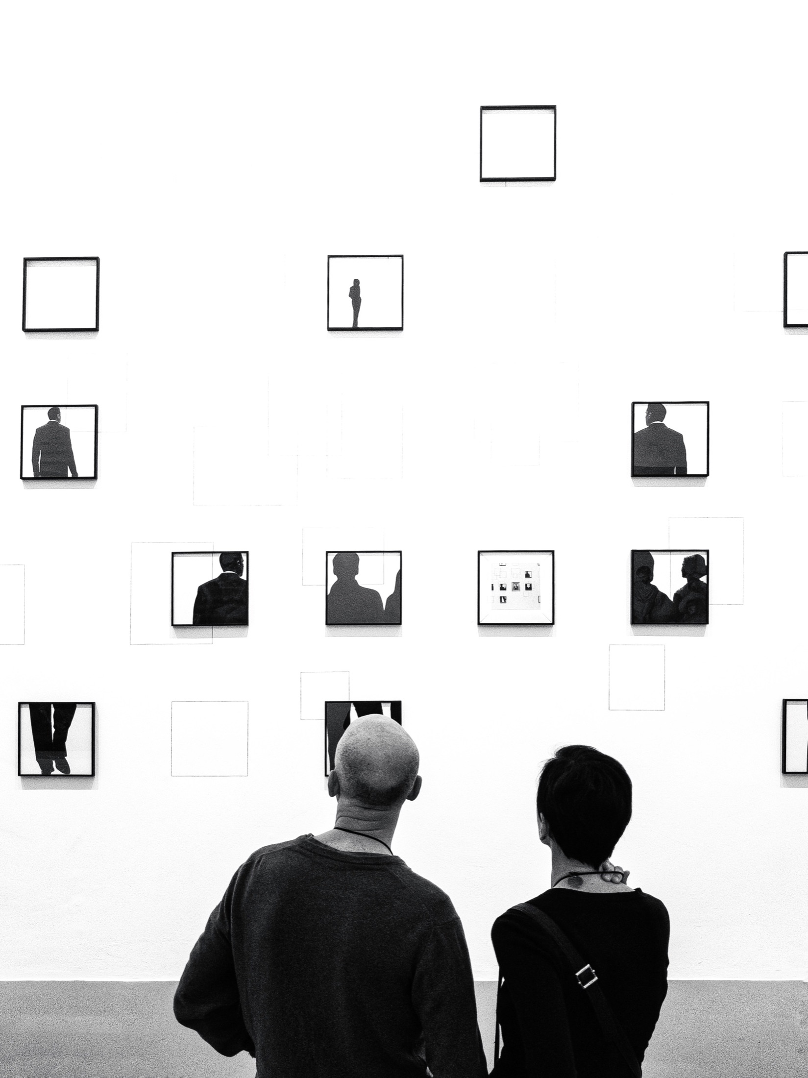 Two people studying a sparse wall of framed art