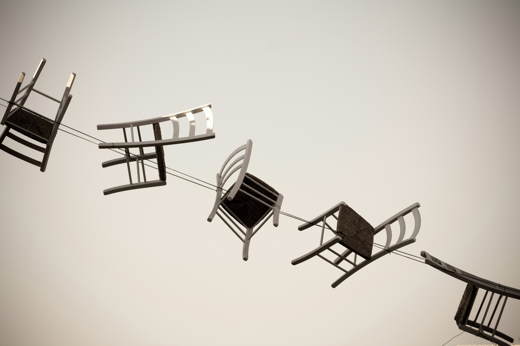 A surreal line of wooden chairs suspended in the sky